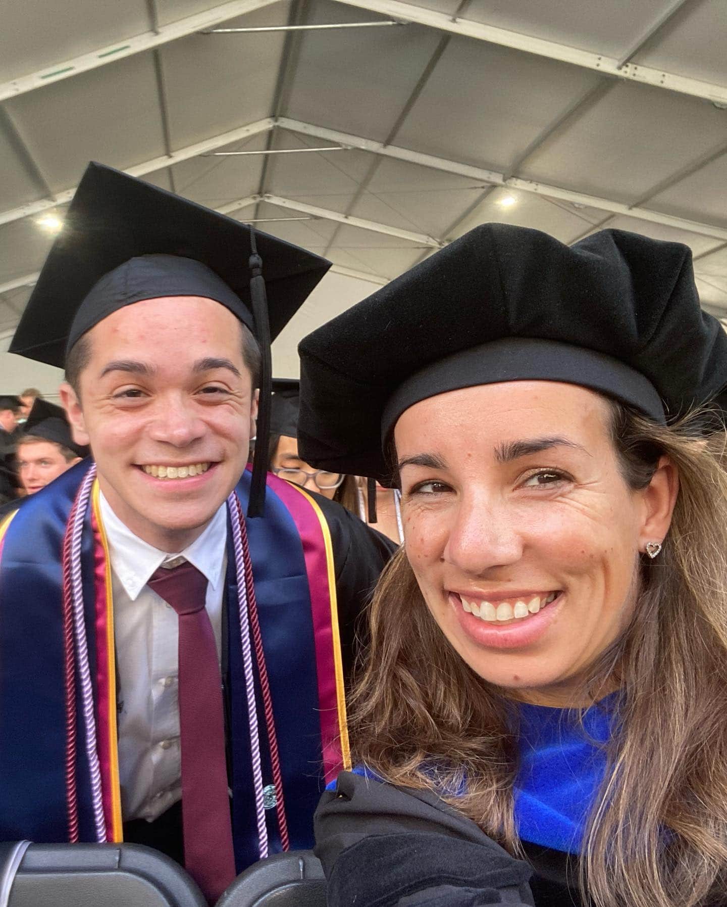 POH_2022_10_Advisee A young white man and a slightly older white woman, both wearing academic dress, smile for the camera at graduation.